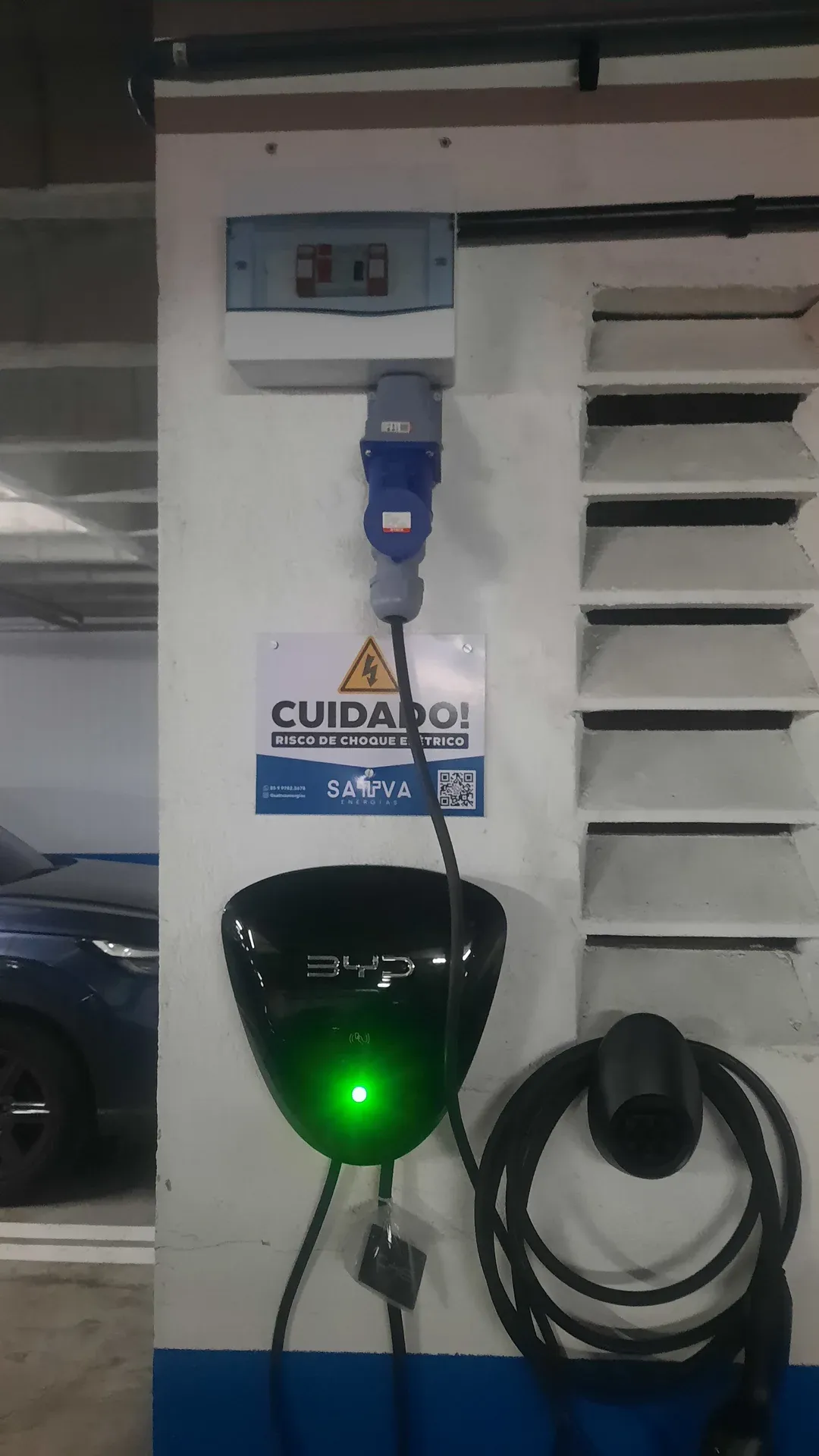 Carregador de carro elétrico instalado em pilar de garagem de condomínio em Fortaleza, com quadro de proteção e sinalização