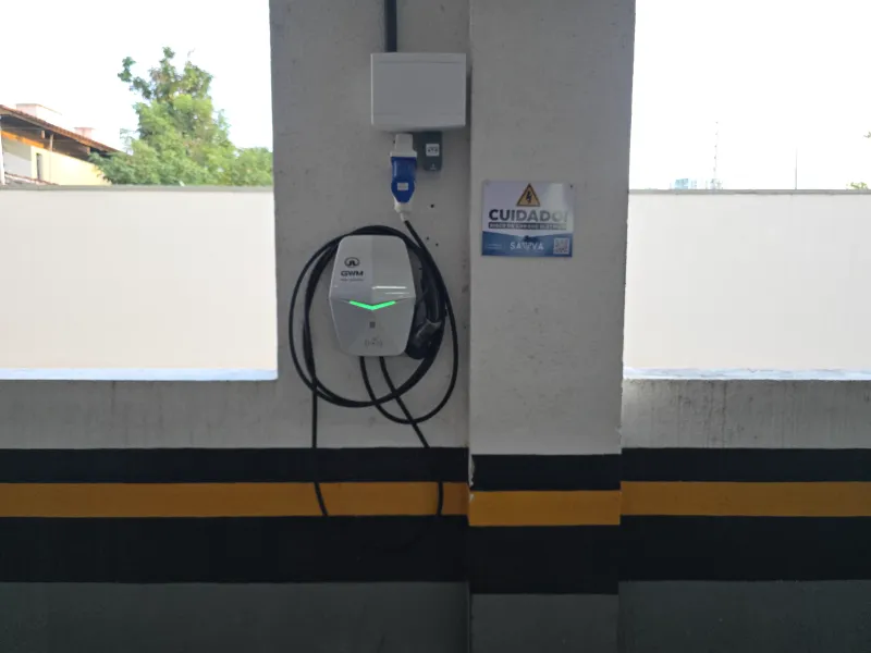 Carregador veicular instalado em coluna de cobertura, com árvores ao fundo