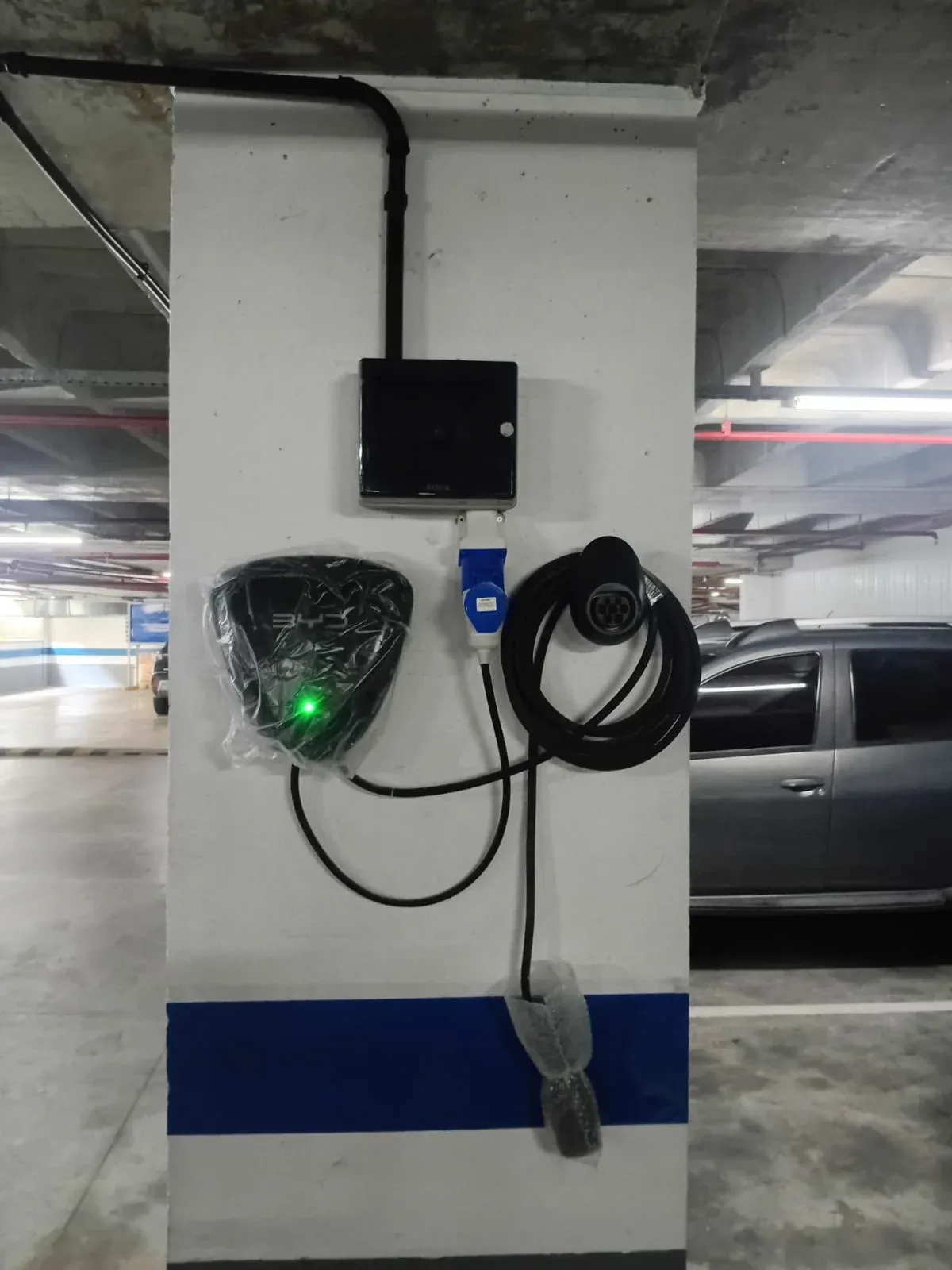 Ponto de recarga veicular em garagem coletiva de condomínio em Fortaleza, com vagas e veículos ao fundo